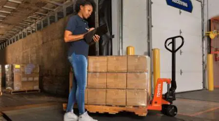 A woman standing in front of boxes and holding a clipboard.