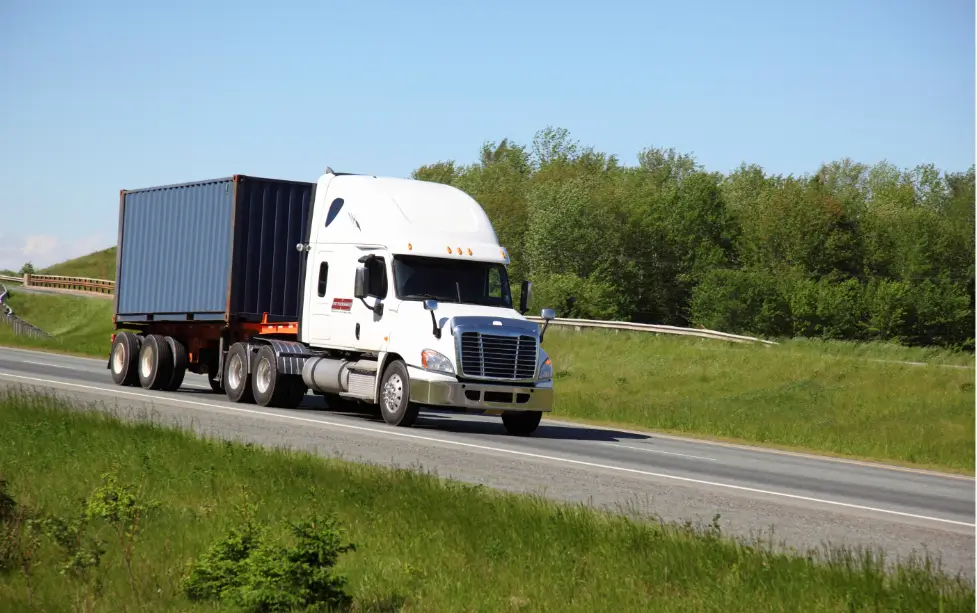 A white semi truck with its trailer on the road.